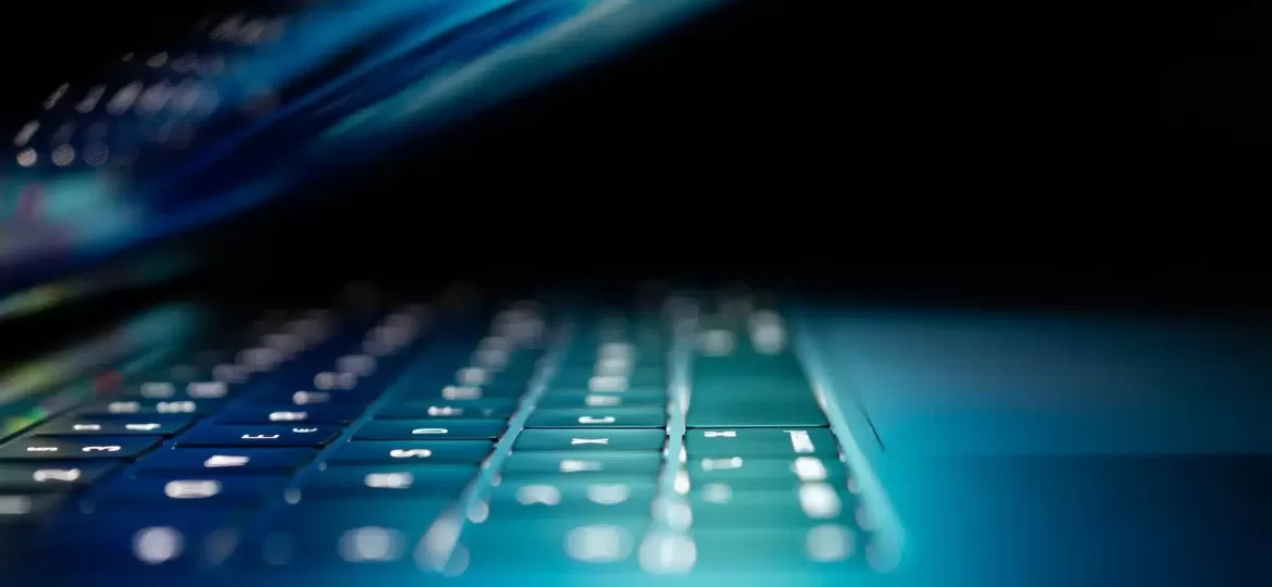 Image of a laptop with the screen half closed, illuminated by blue lights, representing cyber security measures