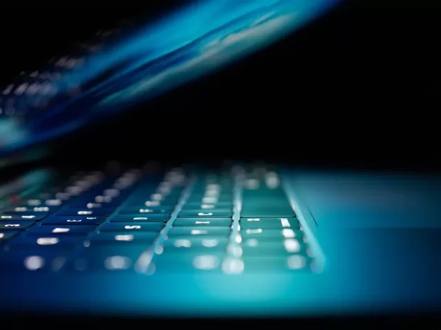 Image of a laptop with the screen half closed, illuminated by blue lights, representing cyber security measures